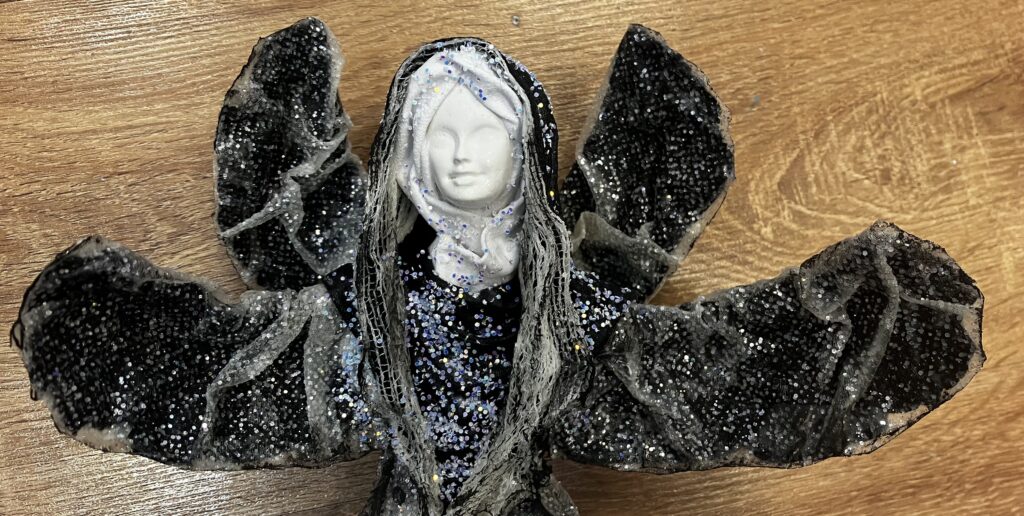 Trblietavý sediaci anjel v čiernom s objímajúcimi rukami👼🏼